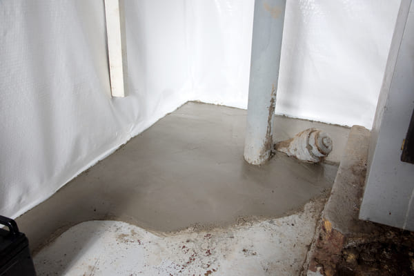 Basement corner with fresh concrete patch and exposed pipes.