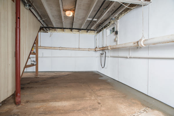 Basement with exposed pipes, white walls, and concrete floor, appearing partially cleaned.