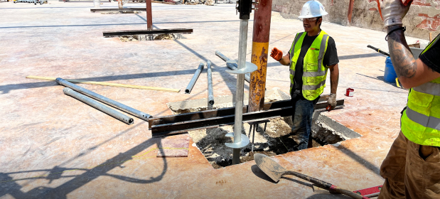 Workers installing a helical pier into a foundation at a construction site.