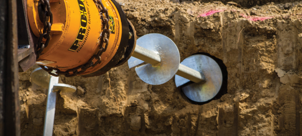 A helical pier being drilled into the ground for foundation support.